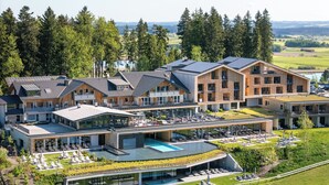A modern hotel with multiple buildings, a swimming pool, and a landscaped garden. - Panorama Allgäu Spa Resort (Rueckholz)