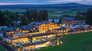 A large, modern hotel with multiple buildings connected by covered walkways, featuring a swimming pool and outdoor seating areas. - Panorama Allgäu Spa Resort (Rueckholz)
