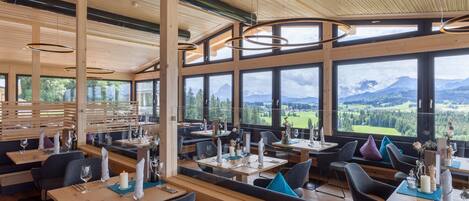 A restaurant with wooden interiors, large windows offering mountain views, and modern pendant lighting.