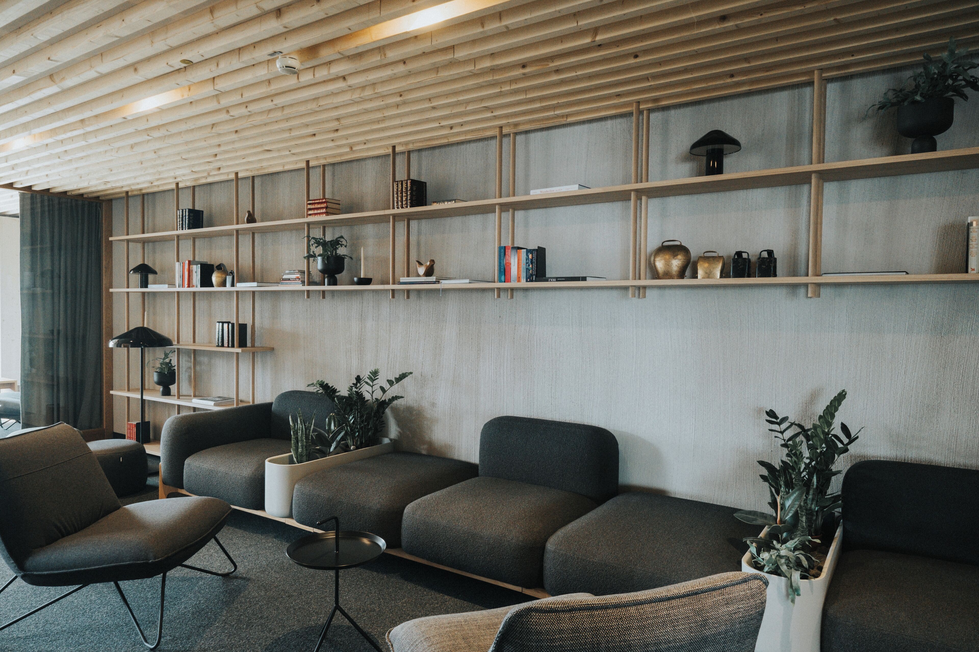 Un salon moderne avec un plafond en bois, des étagères intégrées et des canapés gris.