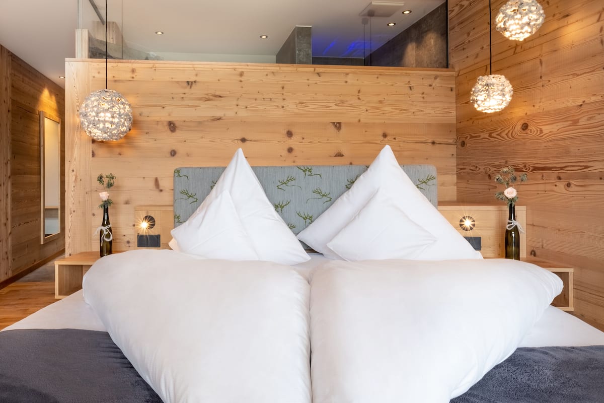 Een moderne slaapkamer met een houten hoofdeinde, twee nachtkastjes met lampen, en een groot bed met witte beddengoed.