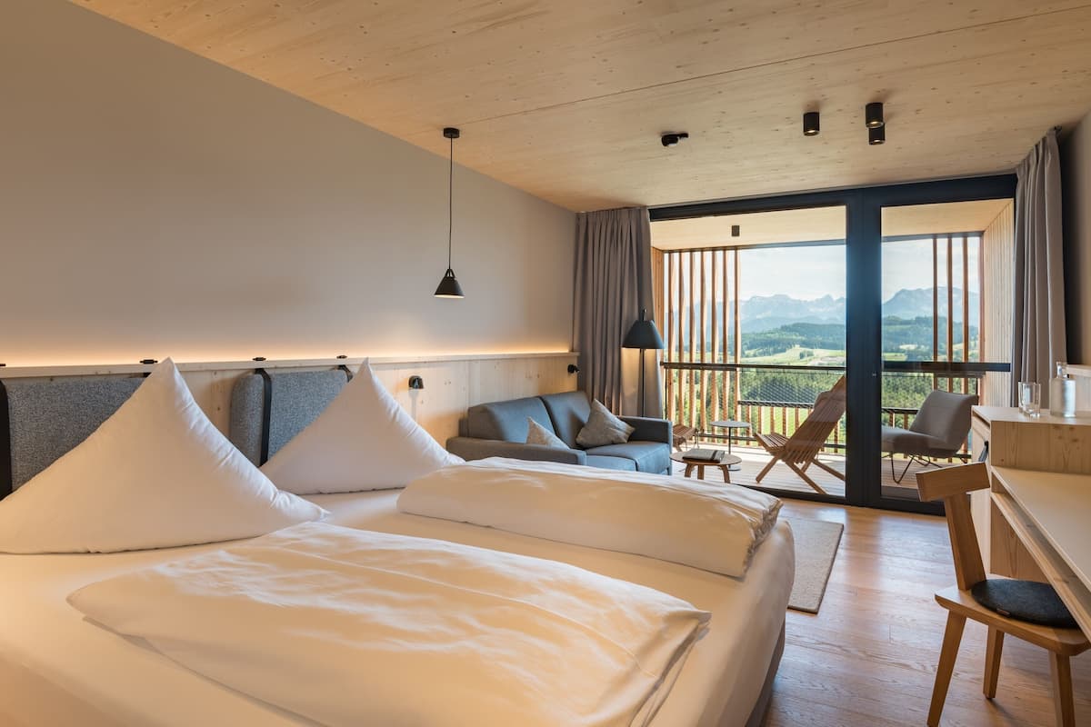 Een moderne hotelkamer met een groot bed, een slaapbank, een bureau en een balkon met uitzicht op de bergen.