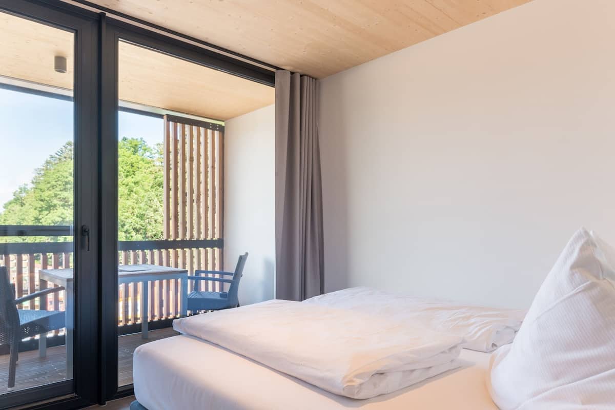 Een hotelkamer met een bed, een stoel en een balkon met uitzicht op bomen.