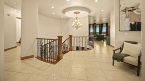 A spacious living area with a staircase, a chandelier, and a large abstract painting on the wall.