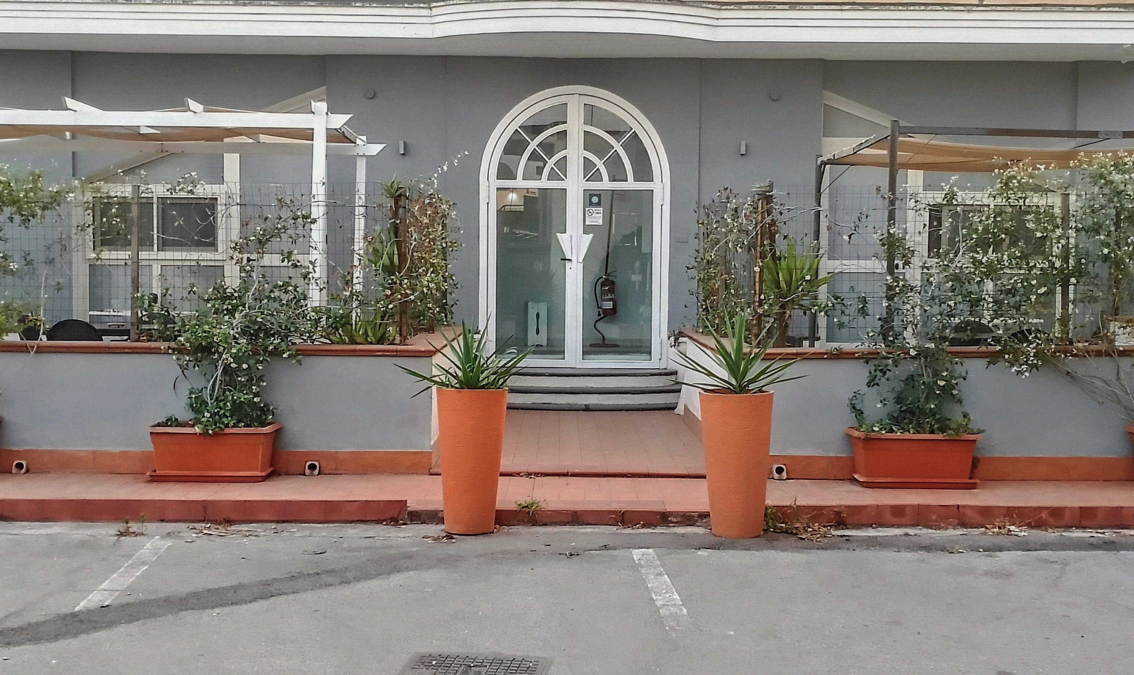 A building with a large arched entrance, potted plants on the ground floor, and a grey facade.
