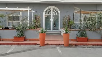 A building with a large arched entrance, potted plants on the ground floor, and a grey facade.