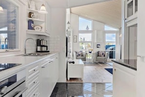 A modern kitchen with white cabinetry, a coffee maker, and a dining area with a table and chairs.