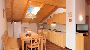 A compact kitchen with wooden cabinets, a dining table with chairs, a built-in oven, and a television on a wooden stand. - Cozy apartment with stunning views of the mountains (Trentino-Alto Adige)