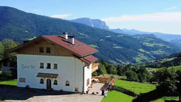 A white building with a red roof, labeled "Stierhof," set against a mountainous backdrop. - Cozy apartment with stunning views of the mountains (Trentino-Alto Adige)