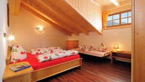 A cozy bedroom with a wooden ceiling, a bed with floral bedding, a bedside table with a book, and a window with a view of mountains. - Cozy apartment with stunning views of the mountains (Trentino-Alto Adige)