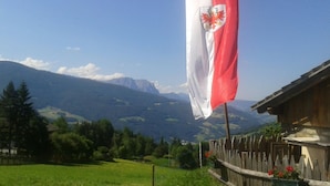 A flag with a red and white design, a wooden fence, and a mountainous landscape in the background. - Cozy apartment with stunning views of the mountains (Trentino-Alto Adige)