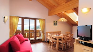 A cozy room with a red sofa, wooden dining table, chairs, a TV, and a balcony with a view. - Cozy apartment with stunning views of the mountains (Trentino-Alto Adige)