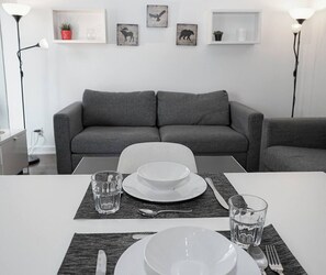 A dining area with a white table set for two, a grey sofa in the background, and wall art depicting animals. - 1BR Condo w/ Balcony/Pool/Gym (Toronto)