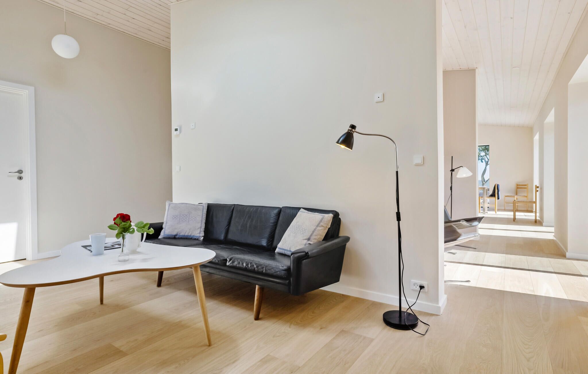 Un salon moderne avec un canapé en cuir noir, une table ronde blanche et un lampadaire.
