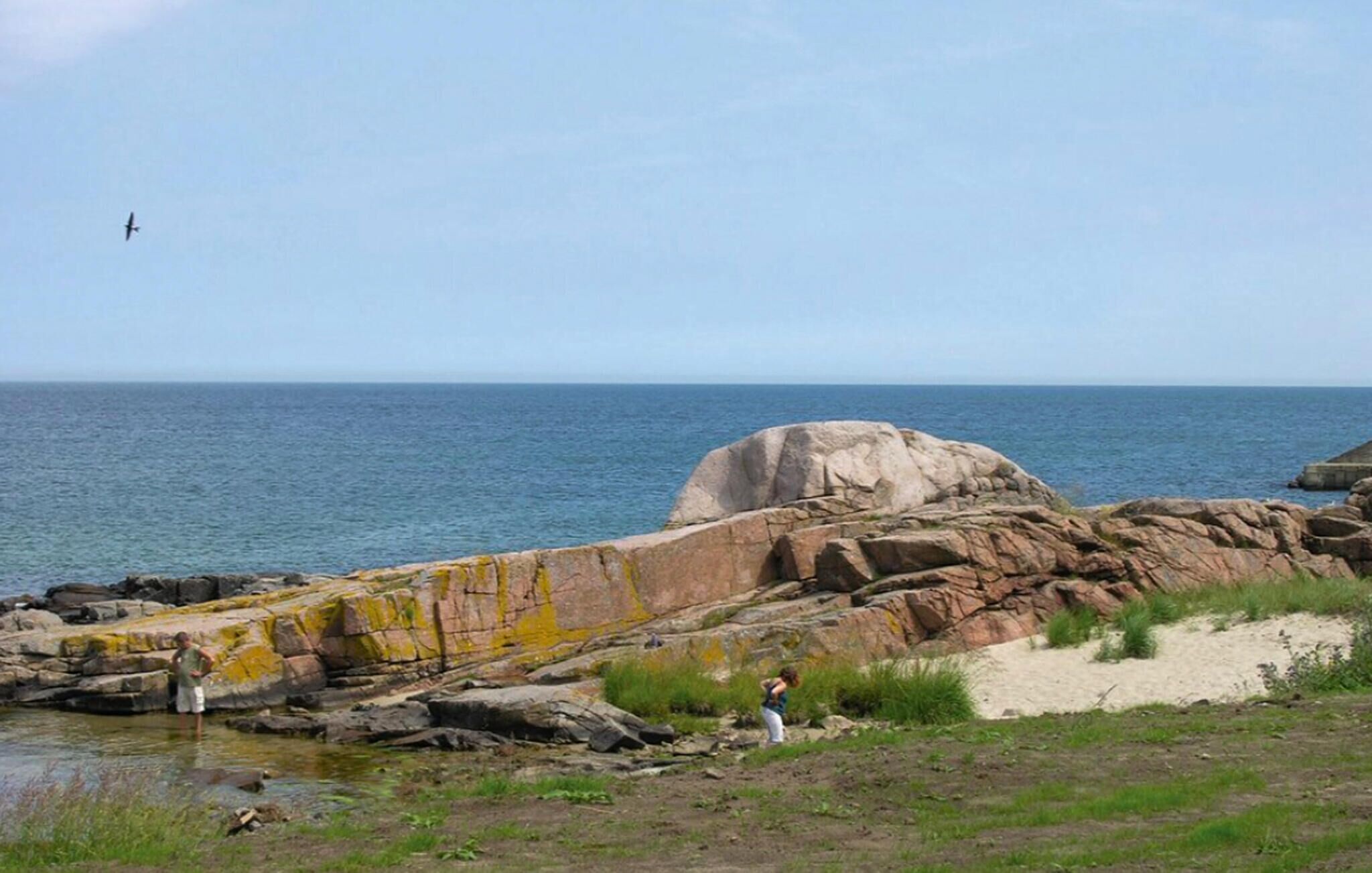 Eine Küstenlandschaft mit großen Felsen, einem Sandstrand und freiem Blick auf das Meer.