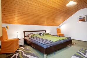 Un dormitorio con techo de madera, una cama con ropa de cama a rayas, una silla, mesitas de noche y una lámpara de pared.