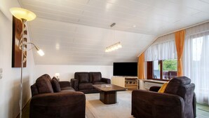 A living room with a sofa set, a coffee table, a TV, and a window with curtains. - Apartment 'Morent' with Mountain View, Balcony and Wi-Fi (Achberg)