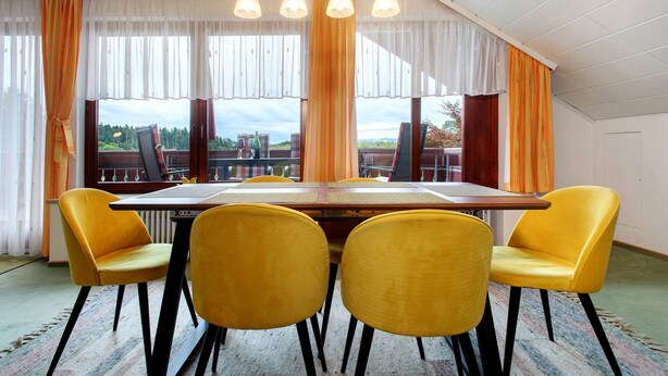 A dining area with a large table, four yellow chairs, and large windows with curtains. - Apartment 'Morent' with Mountain View, Balcony and Wi-Fi (Achberg)