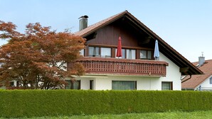 A two-story house with a balcony, a chimney, and a well-maintained hedge in front. - Apartment 'Morent' with Mountain View, Balcony and Wi-Fi (Achberg)