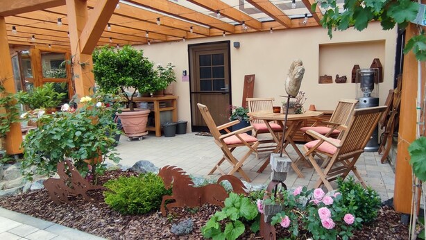 A patio with a wooden pergola, a table with chairs, potted plants, and a decorative metal rooster. - Apartment 'Am Dächsberg' with Private Terrace and Wi-Fi (Plauen)