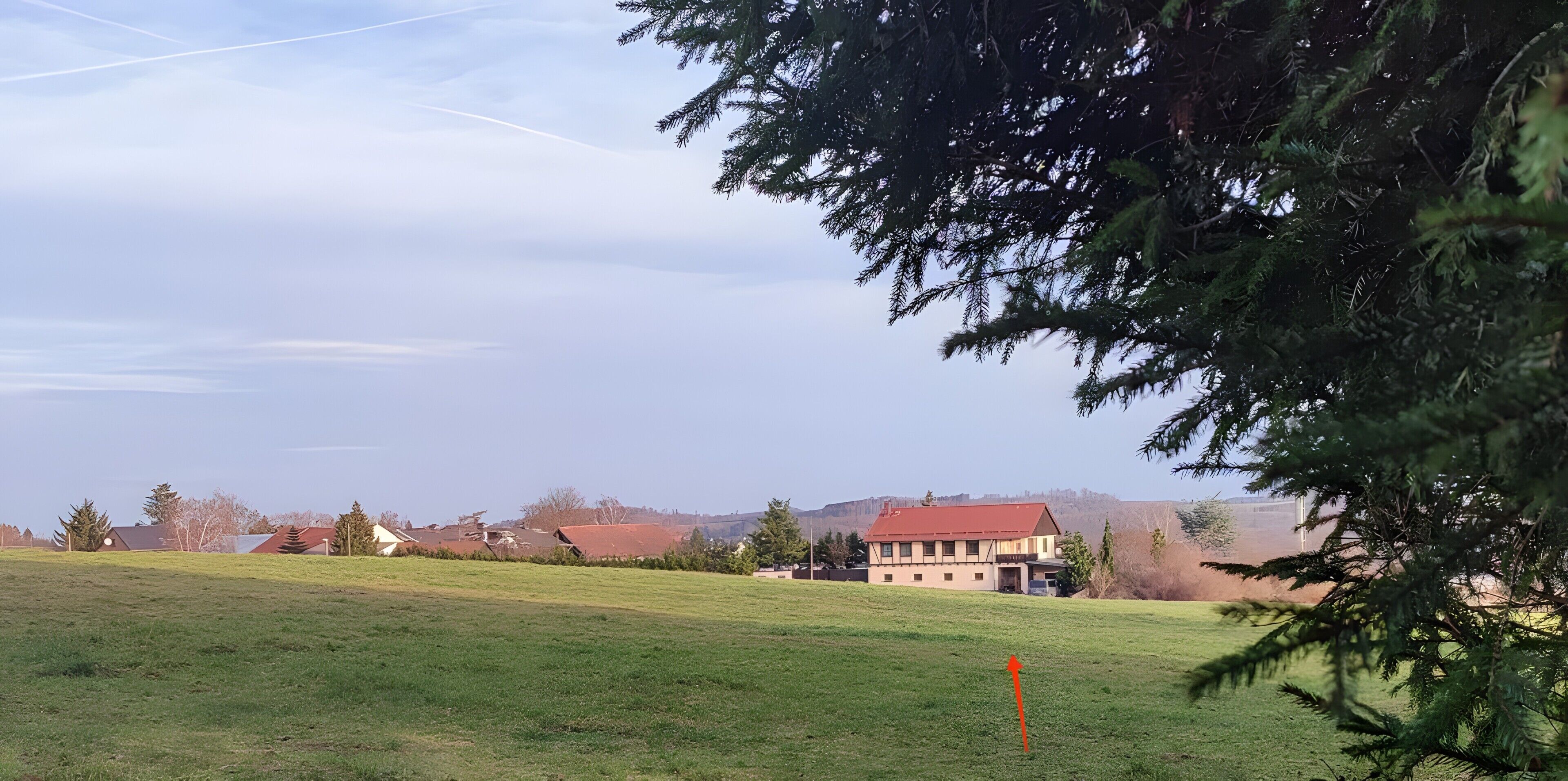 Un campo cubierto de hierba con un edificio de techo rojo y árboles al frente.