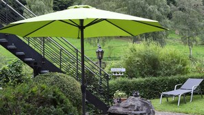 Ein Gartenbereich mit einem grünen Sonnenschirm, einem Metallstuhl, einem Stein und einer Treppe.