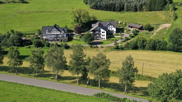 Eine ländliche Landschaft mit einem großen Haus, umgeben von grünen Feldern und Bäumen.
