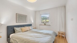 Ein Schlafzimmer mit Bett, Fenster mit Blick, Nachttisch und einem kleinen Holzschemel.