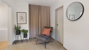 Ein modernes Wohnzimmer mit einem grauen Sessel, einem runden Spiegel und zwei Zimmerpflanzen.
