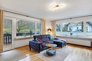 A modern living room with a sectional sofa, a round coffee table, and large windows with curtains. - Apartment 'Stötenberg' with Mountain View, Private Garden and Wi-Fi (Schmallenberg)