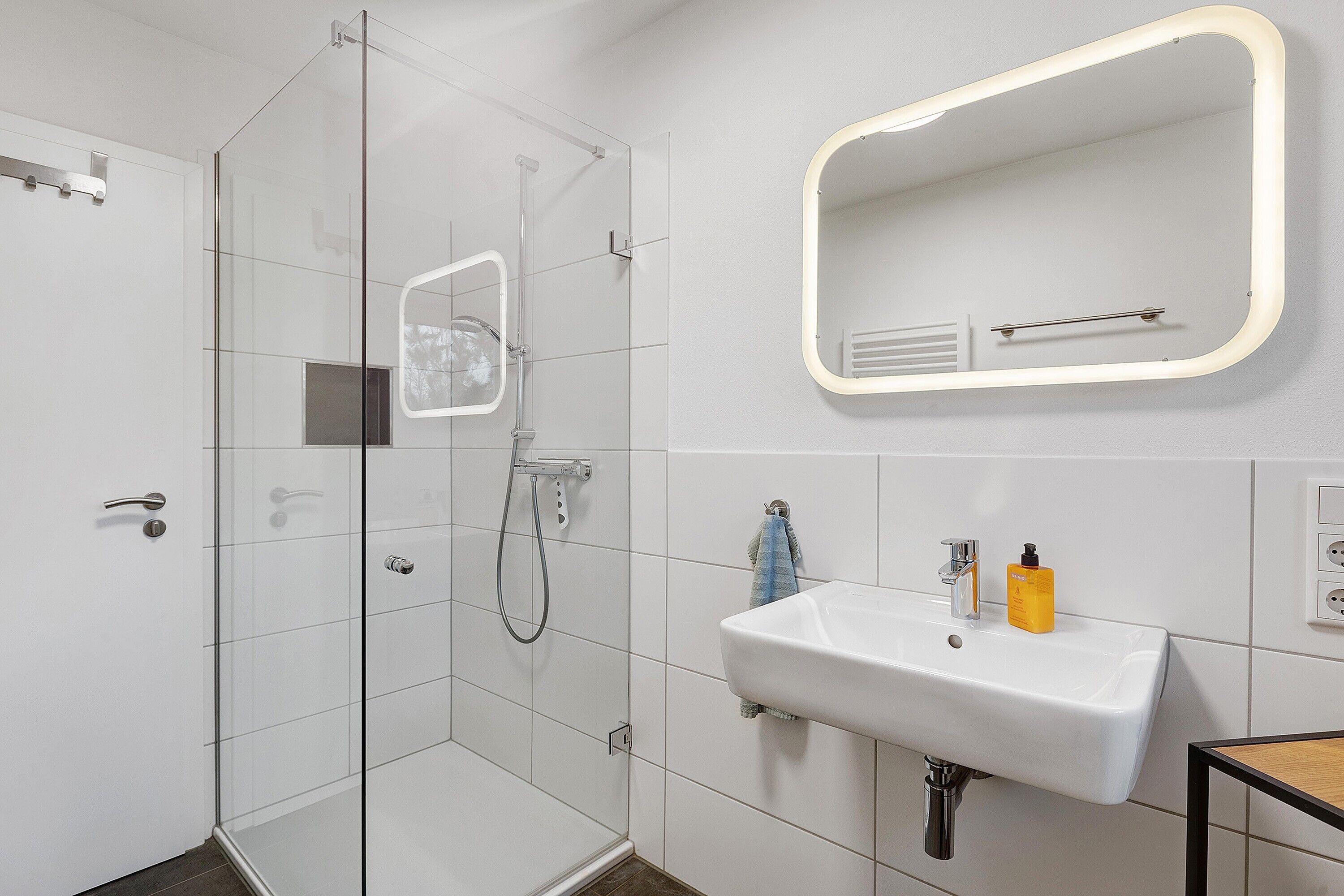 Ein Badezimmer mit Duschabtrennung aus Glas, einem weißen Waschbecken mit Spiegel und einem Handtuchhalter.