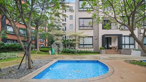 A residential building with a swimming pool, surrounded by trees and greenery.