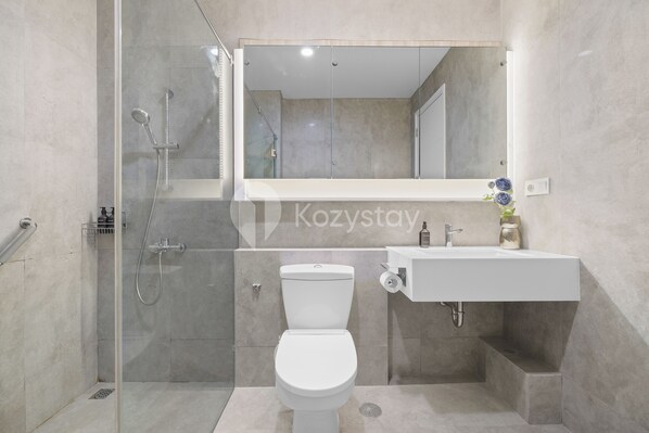Un baño moderno con ducha de vidrio, inodoro y lavamanos con espejo.