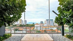 Un balcon avec un fauteuil suspendu, une vue sur le paysage urbain et une végétation luxuriante.