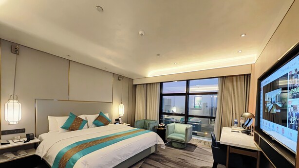 A modern hotel room with a large bed, a desk, a chair, and a TV. - Powerlong Hotel Jinjiang (Quanzhou)