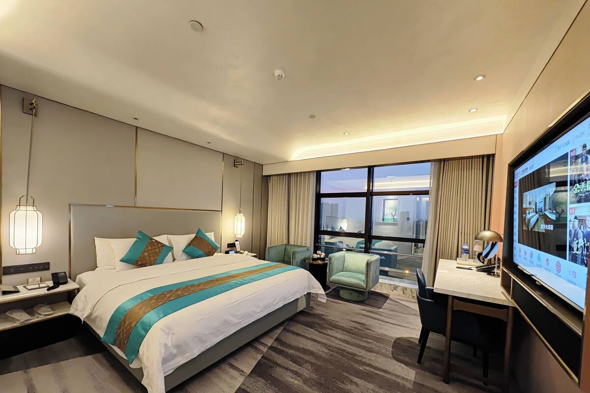 Quarto de hotel moderno com uma cama grande, uma escrivaninha, uma cadeira e uma televisão.