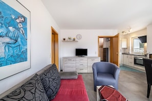 Ein Wohnzimmer mit einer Couch, einem blauen Sessel, einem Flachbildfernseher und einem Bild an der Wand.