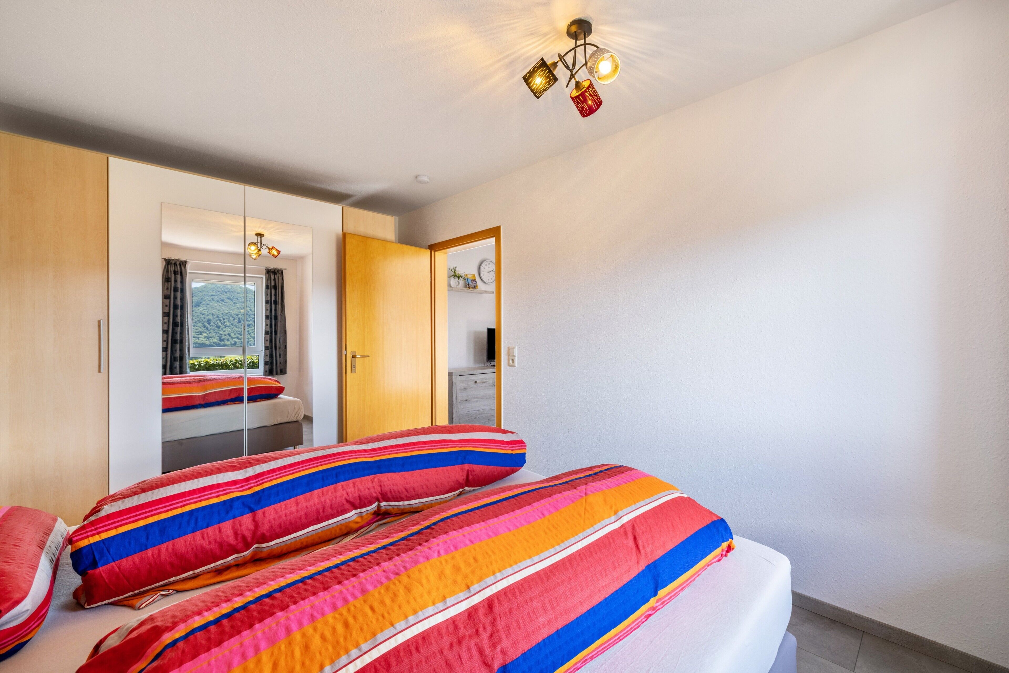 A bedroom with a bed, a wardrobe, a mirror, and a window with curtains.