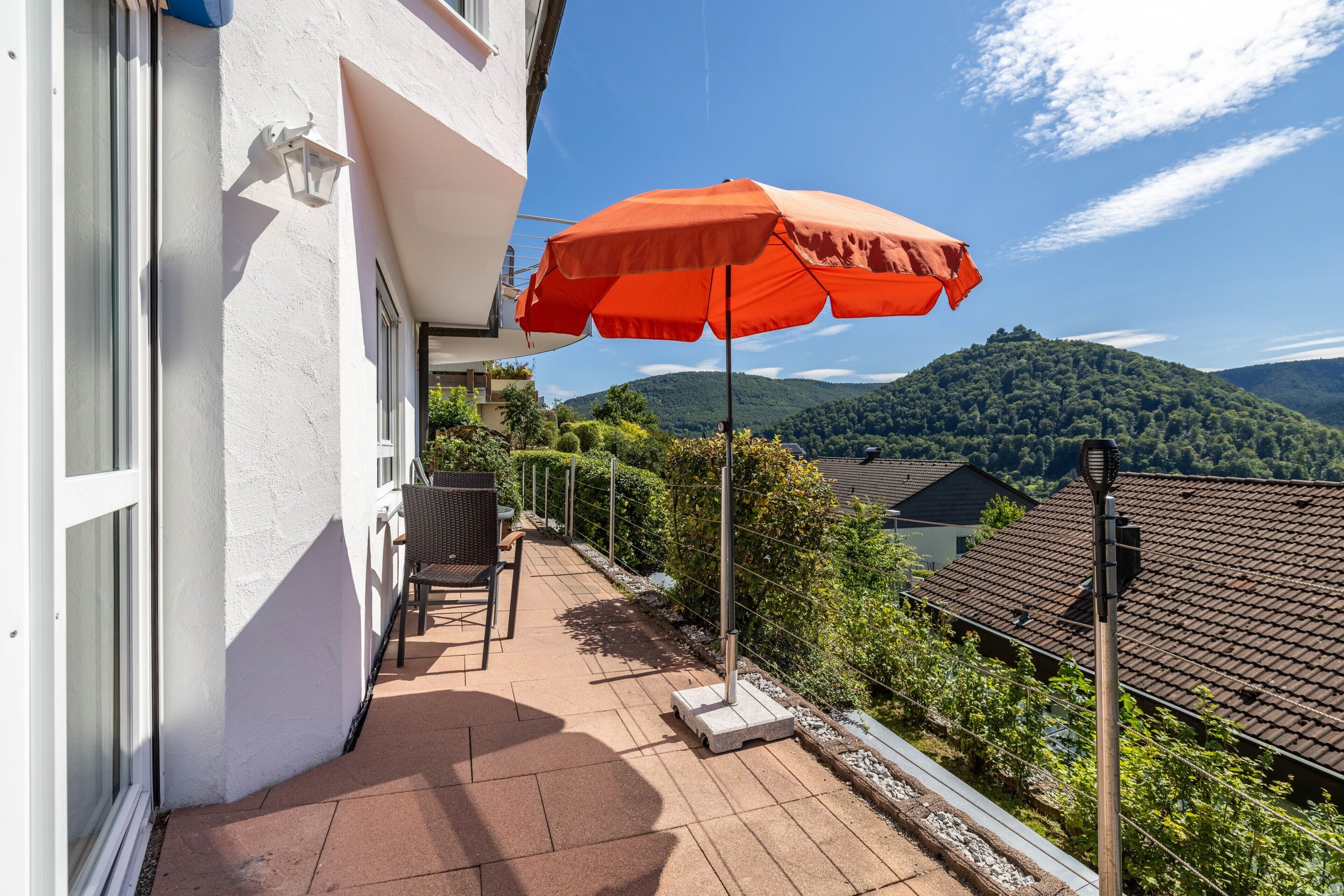 A balcony with a red umbrella, a chair, and a view of a mountain.