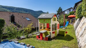 A children's playhouse with a slide, a small table, and a bench in a backyard with a view of a mountain. - Apartment 'Fewo2' with Mountain View, Private Terrace and Wi-Fi (Bad Urach)