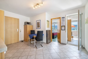 A room with a dining table, chairs, a microwave, a refrigerator, and a door leading to a balcony with a view.