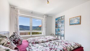 A bedroom with a large window, a bed with floral bedding, a wall-mounted photo display, and a framed picture. - Apartment 'Fewo2' with Mountain View, Private Terrace and Wi-Fi (Bad Urach)