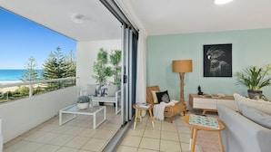 A balcony with a view of the sea, a sofa, a coffee table, and a lamp. - Ambassador Beachfront Apartments (Burleigh Heads)