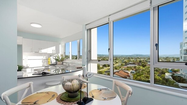 A modern kitchen with white cabinets and a large window overlooking a cityscape. - Ambassador Beachfront Apartments (Burleigh Heads)