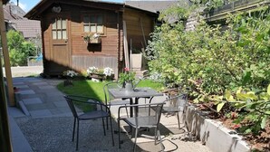Et træhus med en lille terrasse, et bord med stole, og en have med blomster.