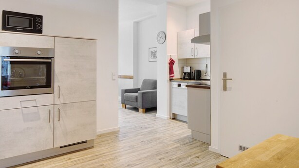 Een moderne keuken met inbouwapparatuur, een eethoek met een houten tafel en een grijze fauteuil.