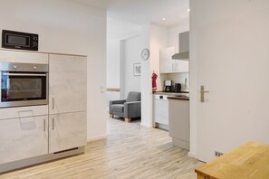 A modern kitchen with built-in appliances, a dining area with a wooden table, and a grey armchair.