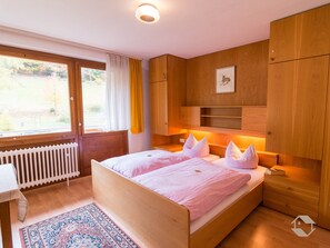 Un dormitorio con cama, ventana, radiador, armarios de madera y una mesita de noche.