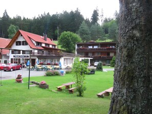 Un hotel con asientos al aire libre, un coche rojo estacionado frente y vistas a una zona boscosa.