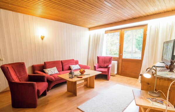 Una habitación acogedora con techo de madera, un sofá rojo, una mesa de centro de madera y un televisor sobre un mueble de madera.